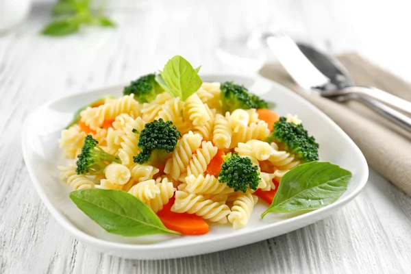 Gekochte Fusilli-Nudeln mit Karotten, Brokkoli und Basilikum auf weißem Teller — Stockfoto