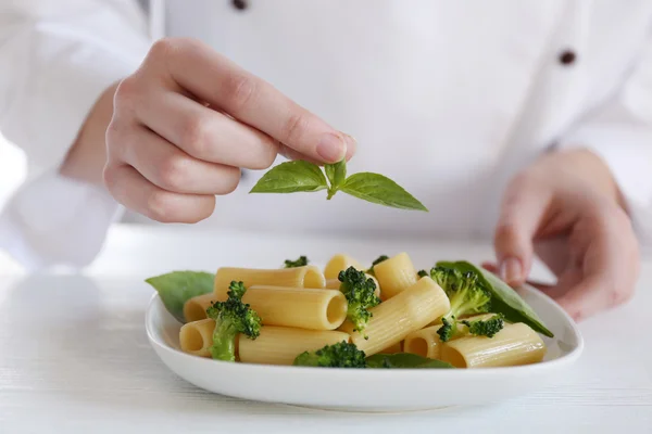 Cocinera decorando pasta rigatoni hervida con brócoli y albahaca en la mesa —  Fotos de Stock