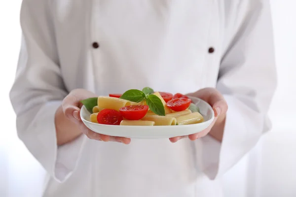 Chef fêmea segurando prato de macarrão rigatoni fervido com tomates frescos e manjericão — Fotografia de Stock