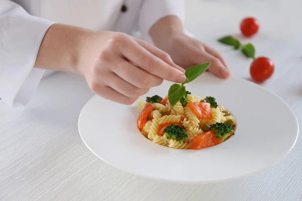 Chef hembra decorando pasta de fusilli hervida con salmón, albahaca y brócoli en la mesa — Foto de Stock