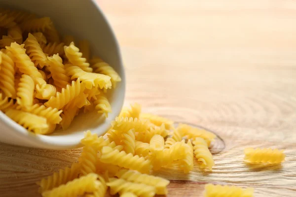 Droge fusilli pasta in witte kom op houten tafel — Stockfoto