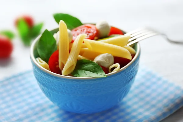 Cooked penne pasta with mozzarella, fresh tomatoes and basil in blue bowl — Stock Photo, Image
