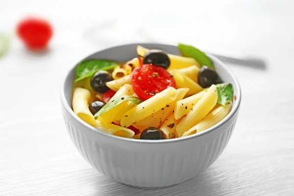 Gekookte penne pasta met olijven, verse tomaten en basilicum in blauwe kom op houten tafel — Stockfoto