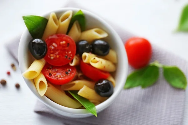 Gekochte Penne-Nudeln mit Oliven, frischen Tomaten und Basilikum in einer weißen Schüssel — Stockfoto