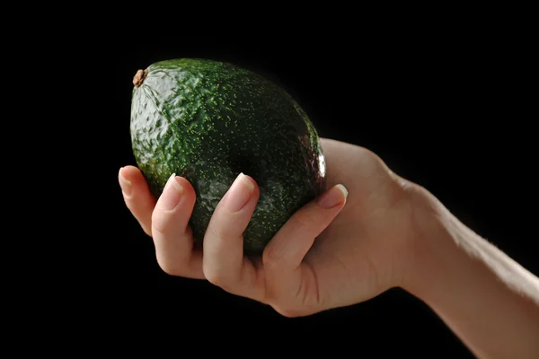 Female hand holding fresh avocado on black background — Stock Photo, Image