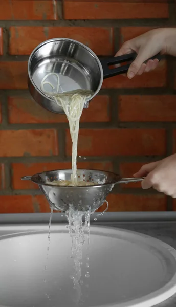 Руки льют воду из кипяченой пасты — стоковое фото