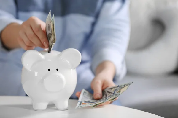 Mão colocando dinheiro no banco porquinho — Fotografia de Stock