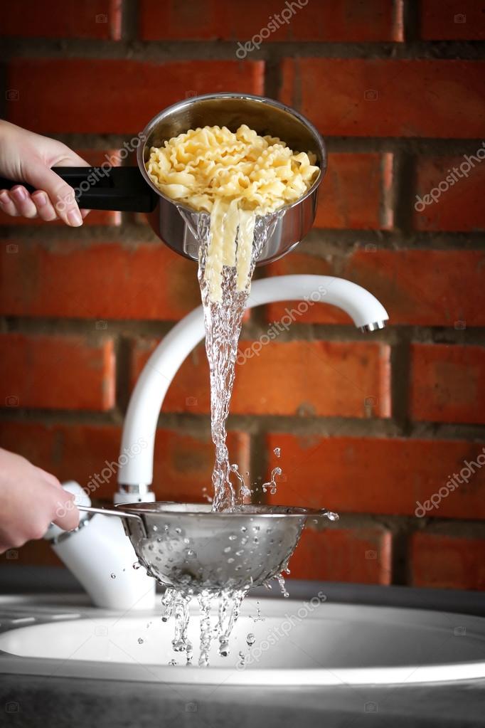 Hands pouring water from boiled pasta Stock Photo by ©belchonock 108395078