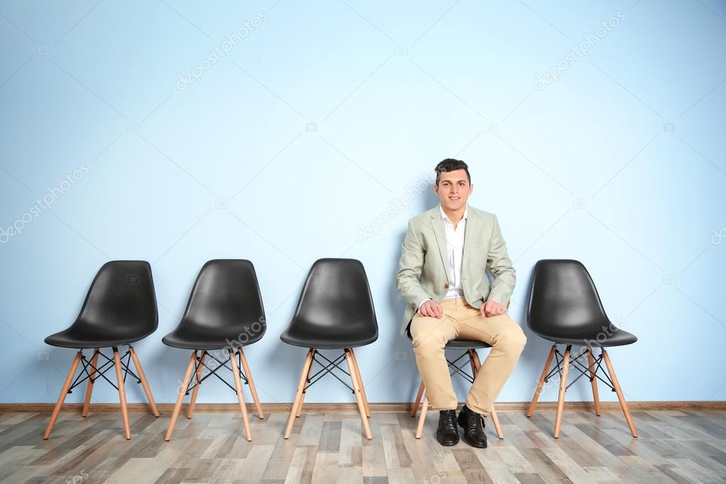 Young man in suit sitting on chair and waiting for job interview