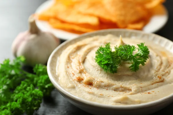 Tazón de cerámica de sabroso hummus con papas fritas y perejil en la mesa — Foto de Stock