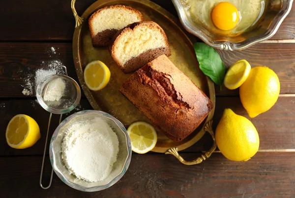 Delicious sweet cake bread in metal tray with lemons on wooden table, top view — Stock Photo, Image