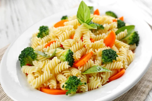 Pasta fusilli bollita con carota, broccoli e basilico su piatto bianco — Foto Stock