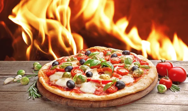 Delicious hot pizza on wooden table against fire flame background — Stock Photo, Image