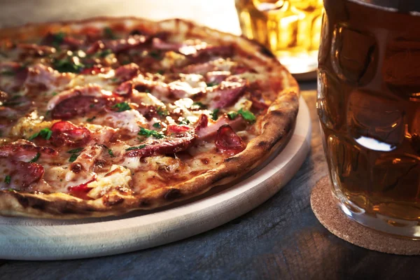 Deliciosa pizza y vasos de cerveza están en la mesa de madera, de cerca — Foto de Stock