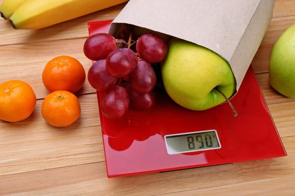 Fresh fruits on red digital kitchen scales — Stock Photo, Image