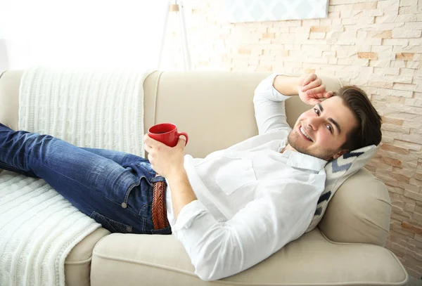 Мужчина лежит на диване с чашкой — стоковое фото