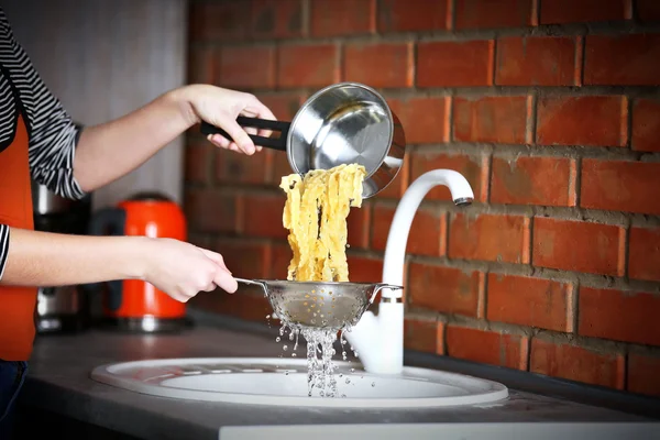 Hands pouring water from boiled pasta — Stock Photo, Image