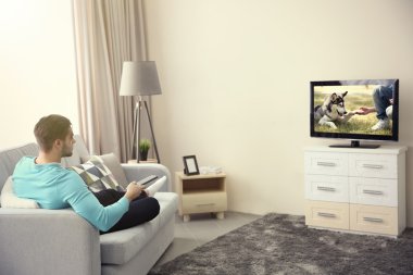 Genç adam evde televizyon izliyor.