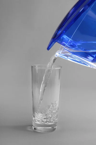 Jarro de filtro derramando água no vidro — Fotografia de Stock