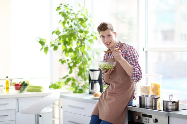 Uomo che mangia insalata di verdure in cucina — Foto Stock