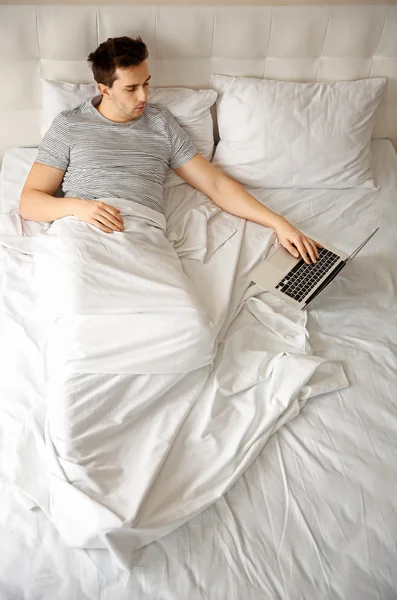 Man liggend in bed met laptop — Stockfoto