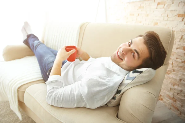 Мужчина лежит на диване с чашкой кофе — стоковое фото