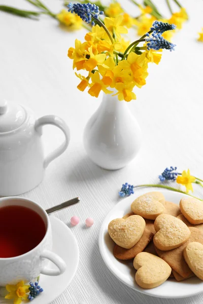 Narcissus flowers with cup of tea and cookies — Stock Photo, Image