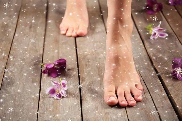 Kvinnliga fötter och blommor på trä bakgrund — Stockfoto