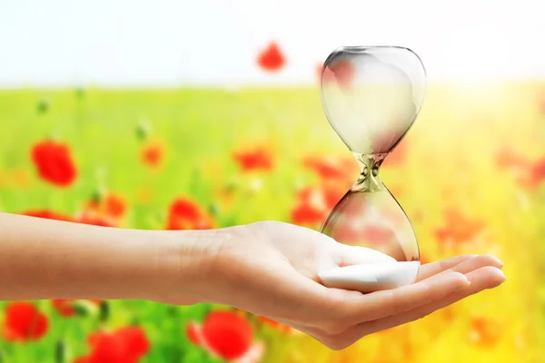 Hourglass in female hand on field — Stock Photo, Image