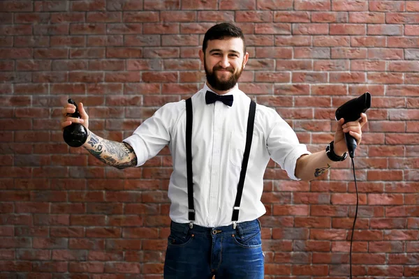 Cabeleireiro profissional com secador de cabelo e spray no fundo da parede de tijolo — Fotografia de Stock