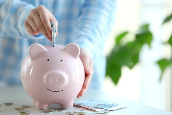 Woman putting money in piggy bank — Stock Photo, Image