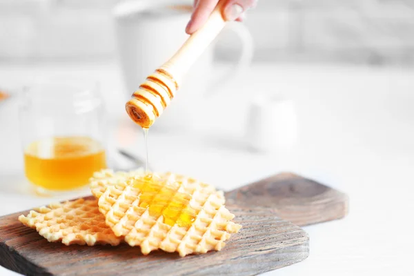 Mão feminina derramando mel em waffles — Fotografia de Stock