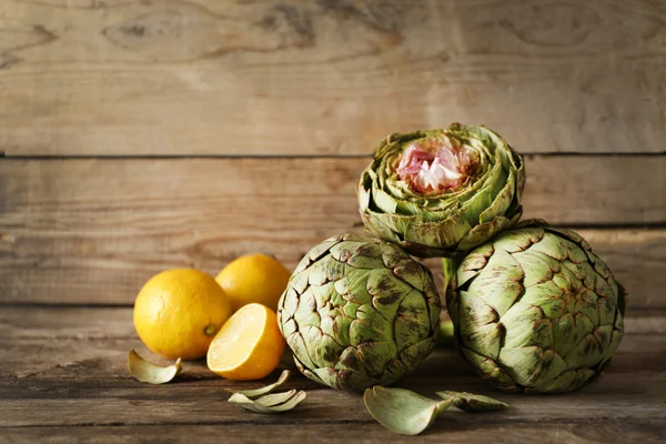 Alcachofa con limones sobre madera — Foto de Stock