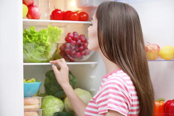 Ung kvinna står bredvid kylskåpet — Stockfoto