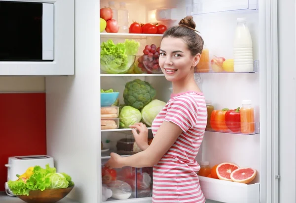 Ung kvinna står bredvid kylskåpet — Stockfoto