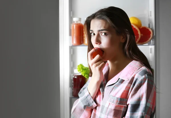 Frau isst Tomate aus Kühlschrank — Stockfoto