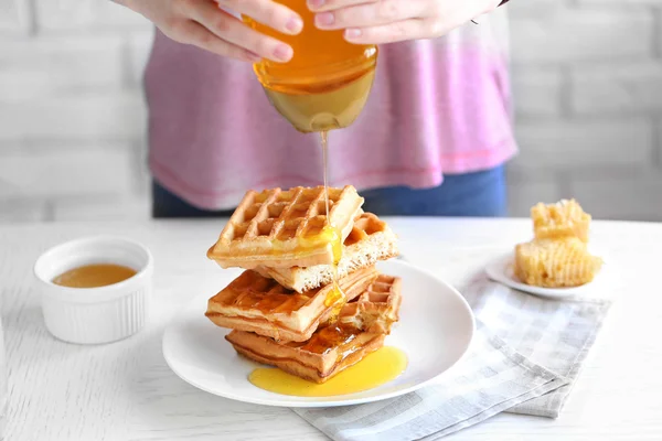 Woman pouring honey on waffles — Stock Photo, Image