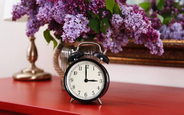 Alarm clock with lilac bouquet — Stock Photo, Image