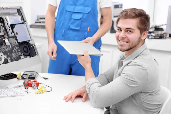 Young man giving broken laptop to repairer in service center — Stock Photo, Image