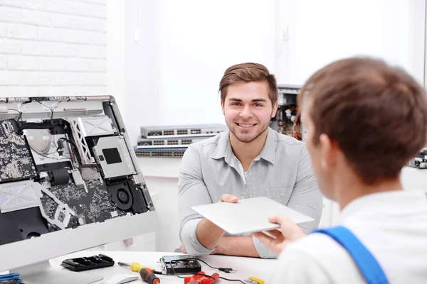 Young man giving broken laptop to repairer in service center — Stock Photo, Image