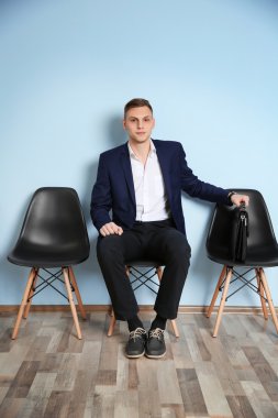 Sandalyede oturan ve iş görüşmesi için bekleyen elbiseli genç adam