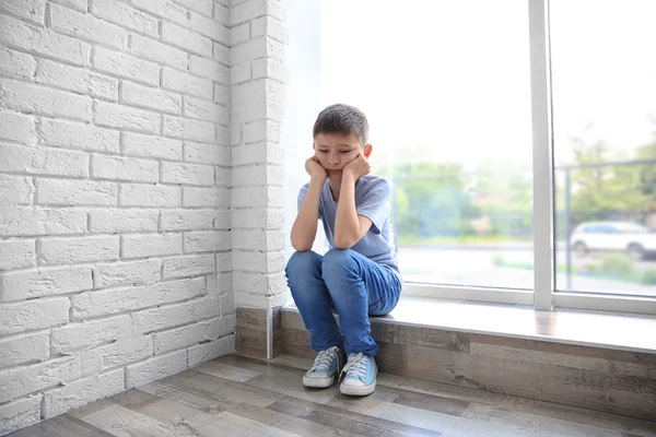 Грустный мальчик сидит у окна — стоковое фото