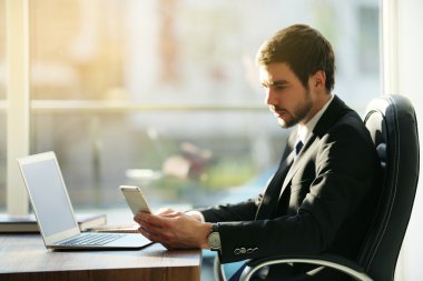 Ofiste cama tabloda, dizüstü bilgisayar ve akıllı telefon kullanan adam