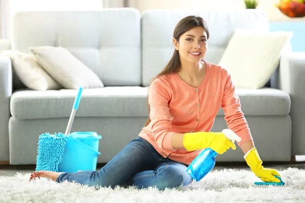 Schöne Frau in Schutzhandschuhen putzt Teppich mit Pinsel und Spray — Stockfoto
