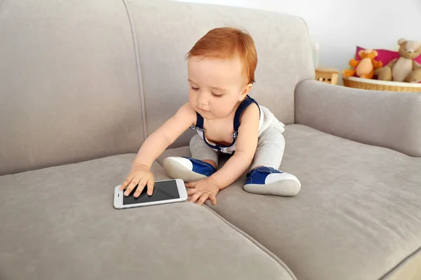 Красивый ребенок играет с телефоном на диване — стоковое фото