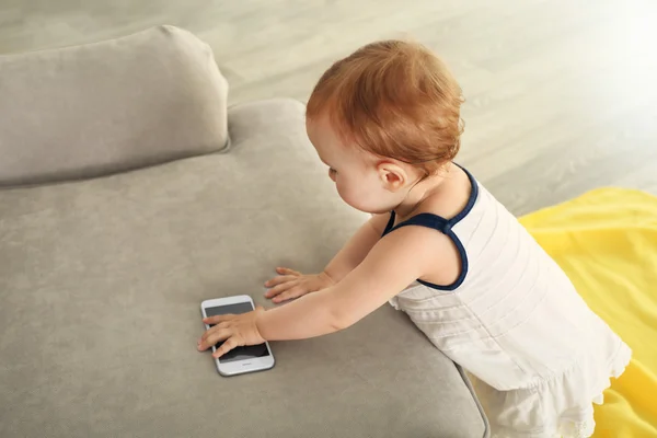 Beautiful Baby touching telephone on sofa — Stock Photo, Image