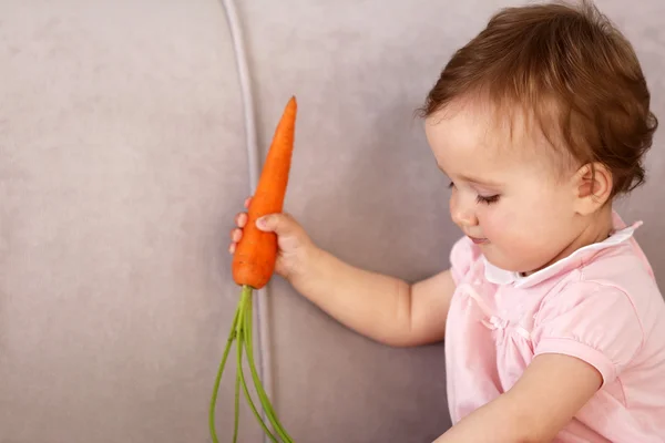 Beautiful Baby with carrot on sofa in room Stock Photo