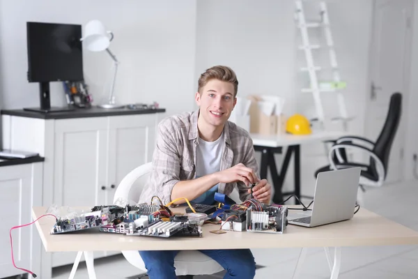 Nuori mies korjaamassa tietokonelaitteita huoltokeskuksessa — kuvapankkivalokuva