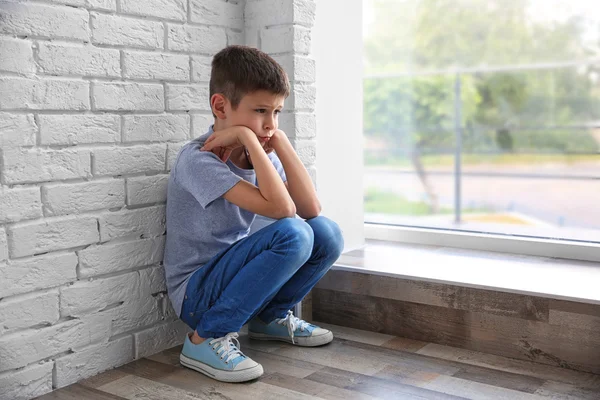 Грустный мальчик сидит у окна — стоковое фото