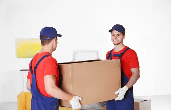 Trabajadores masculinos con caja y muebles en casa nueva — Foto de Stock